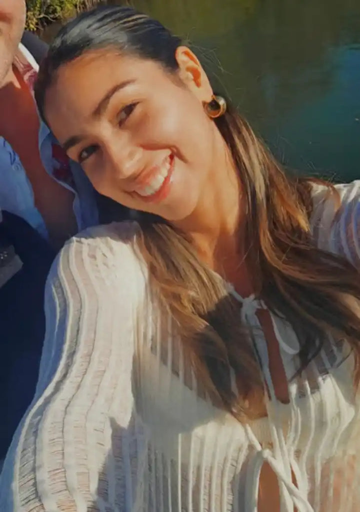 A smiling woman with long brown hair wearing a sheer white long-sleeve top.
